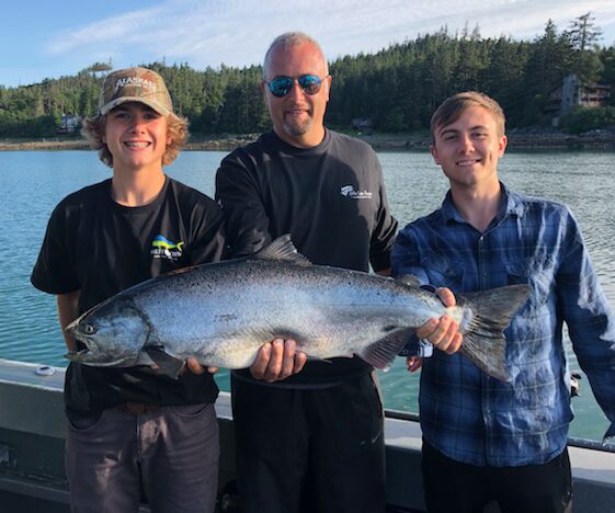 Three people holding a large silver salmon on a boat deck in Juneau, Alaska.